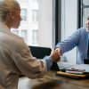 Two professionals in an office setting shaking hands after a business agreement.