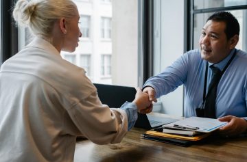 Two professionals in an office setting shaking hands after a business agreement.